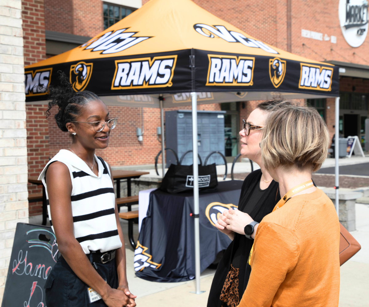 3 women talking in front of a vcu rams tent